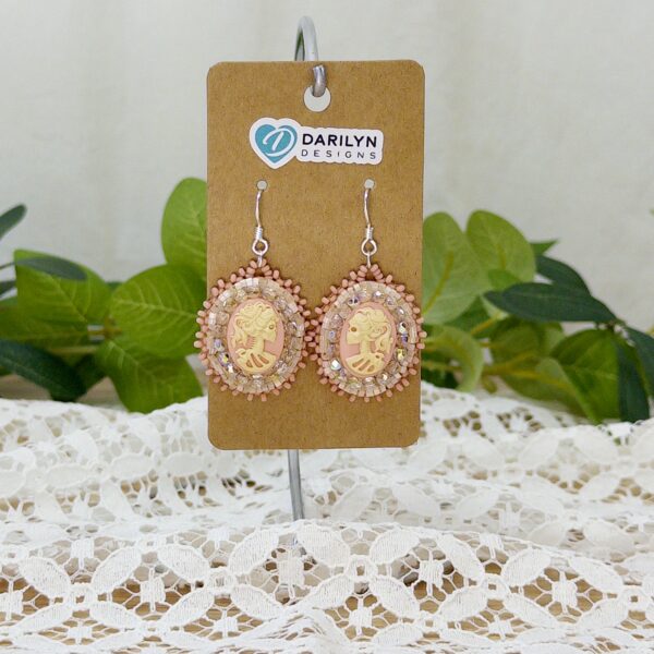 Pink beaded earrings featuring a skeleton cameo hanging from a stand.