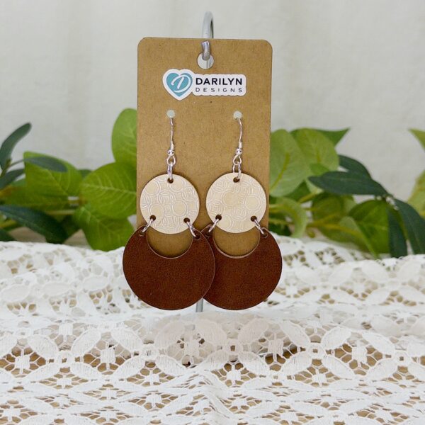 Silver-foiled birch and faux suede geometric earrings hanging from a stand.