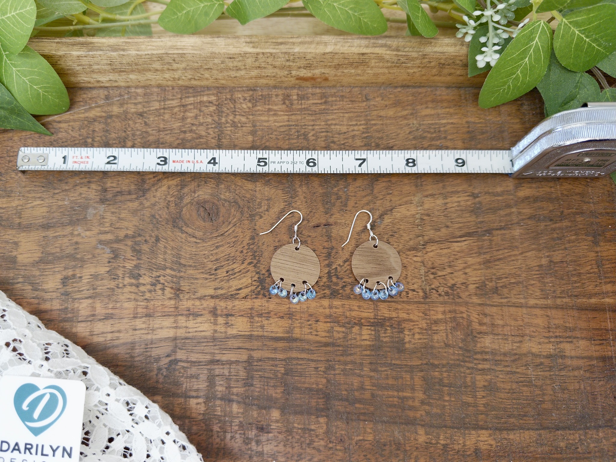 Round wood earrings with blue glass bead fringe show with a ruler.