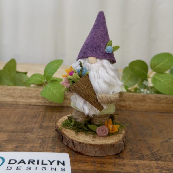 Front view of Bruce, a Gnome wearing purple and green holding a tiny bouquet of flowers.