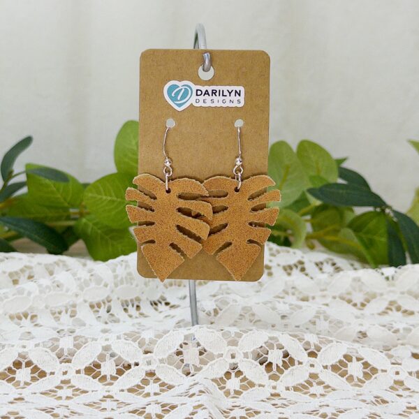Faux suede monstera earrings hanging from a stand.