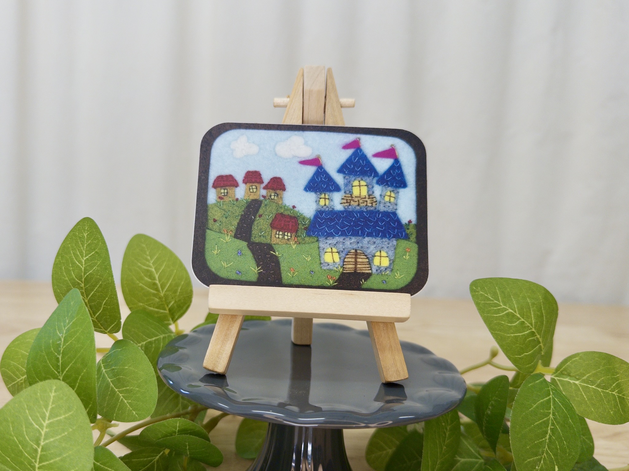 A vinyl sticker showing a castle and small village displayed on a small wooden easel.