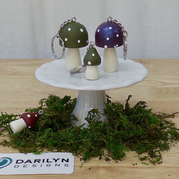 Mushroom keychains displayed on a small white stand with moss.