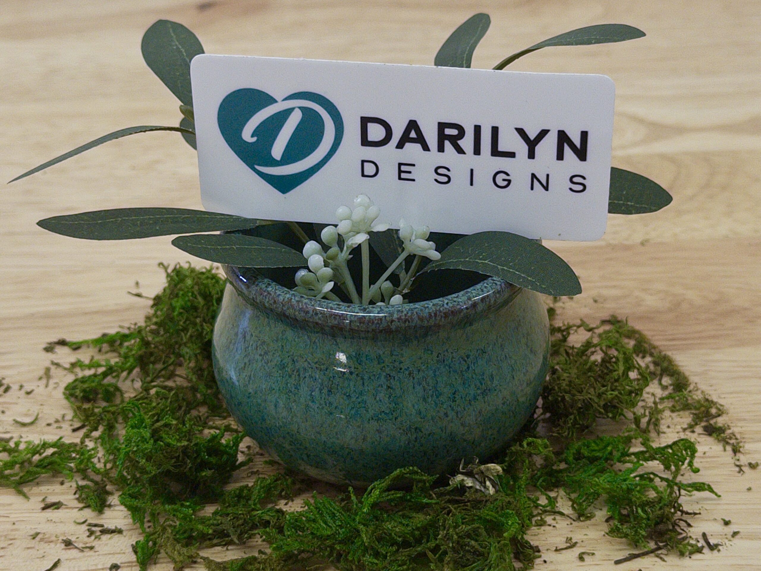 A hand holding a miniature terracotta pot with a felt lavender bush.