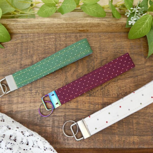 Three cotton wristlets in green, berry, and white on a wood board.
