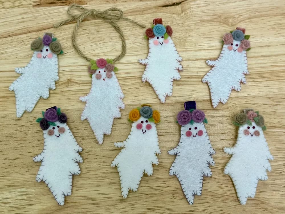 Eight handmade felt ghost purse charms with felt flower crowns, laid out on a wood table