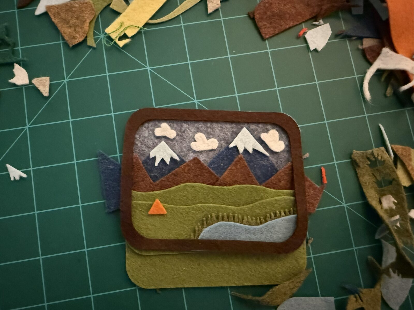 A framed felt mountain scene with snowy peaks and white flowers