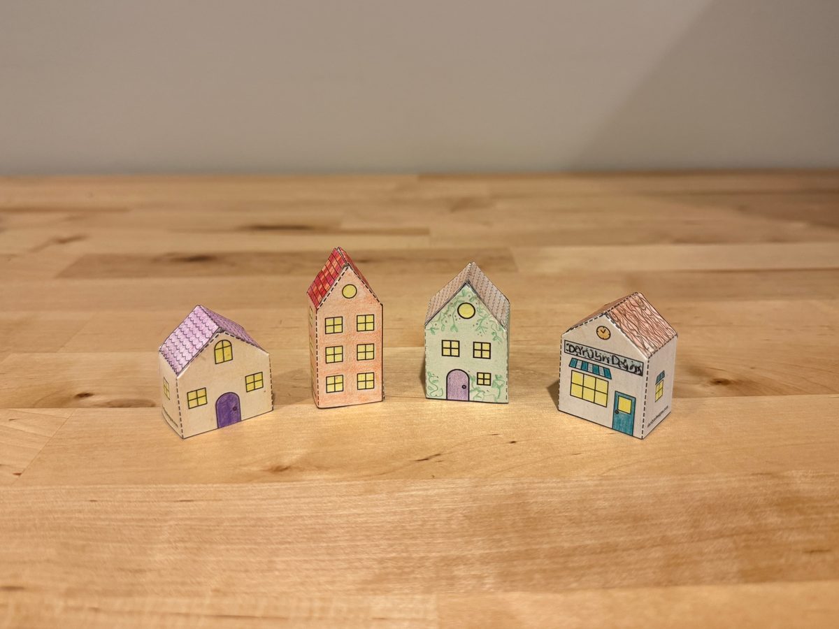 All four paper houses built and colored, standing in a row on a wooden counter