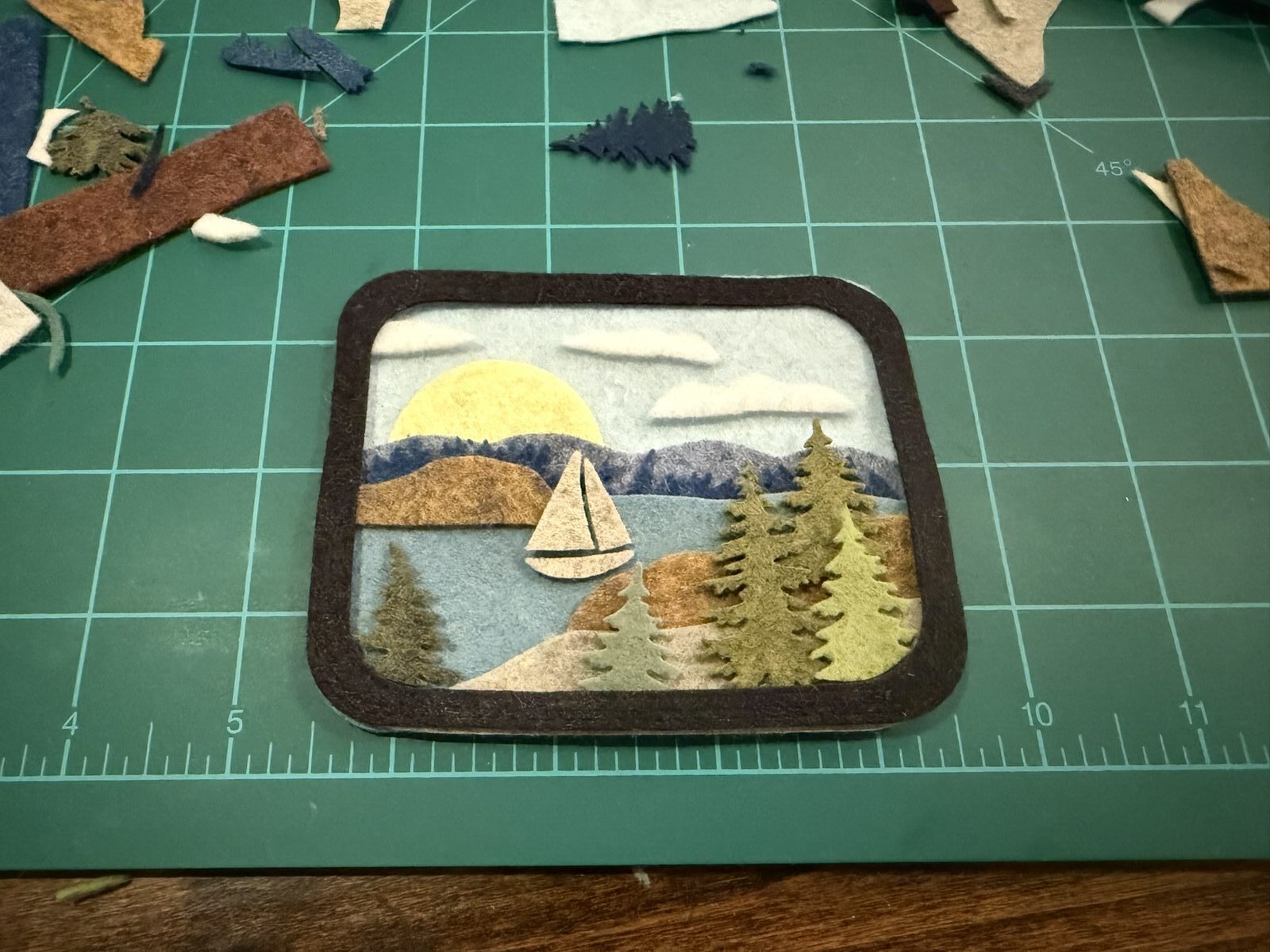 A framed felt sailboat scene with a moon and trees