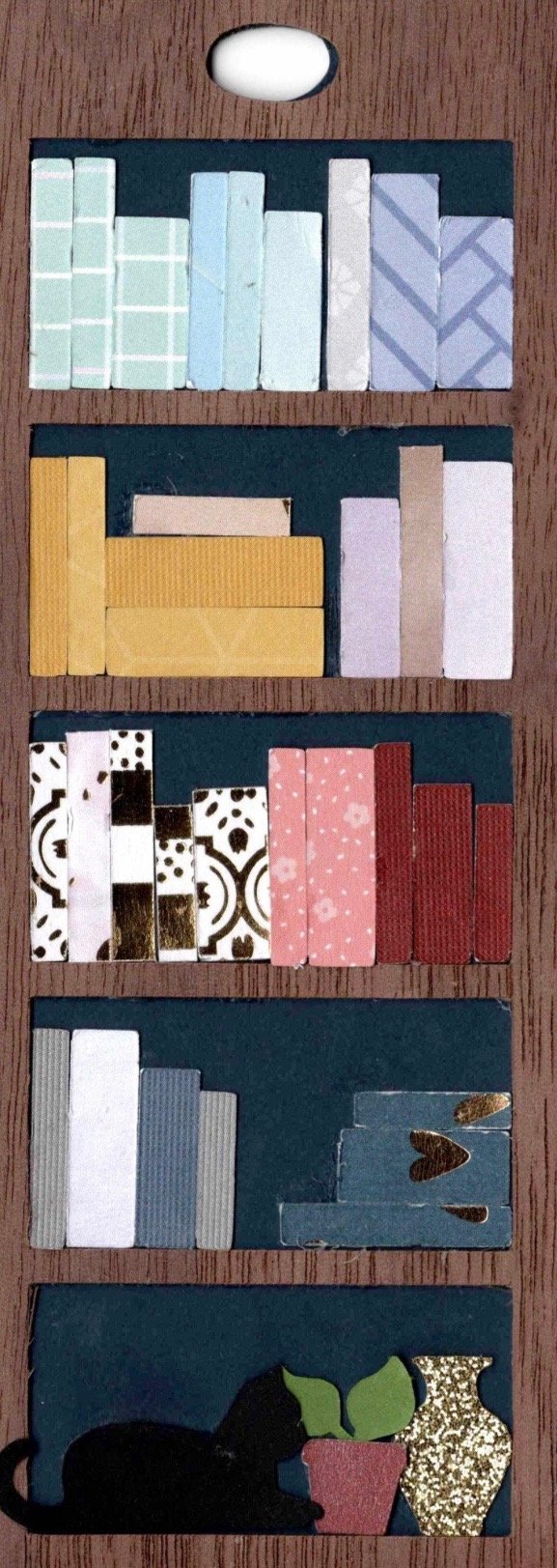 Mini Bookshelf Bookmark styled with every shelf packed full of paper books, grouped by color, with a black cat on the bottom shelf