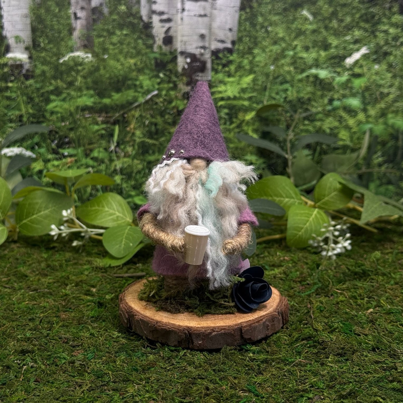 One-of-a-kind handmade felt gnome with a tall purple hat, photographed among green leaves