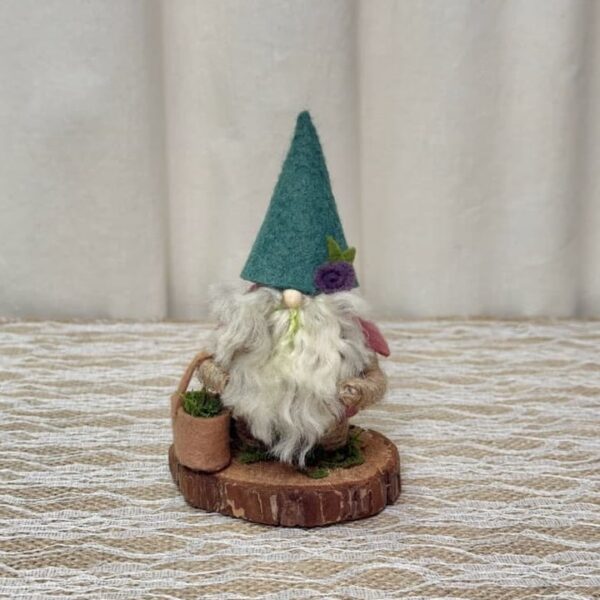 Earl, a handmade gnome with a teal felt hat, purple felt rose, moss in his white yarn beard, and a tan felt basket of moss on a wood slice base