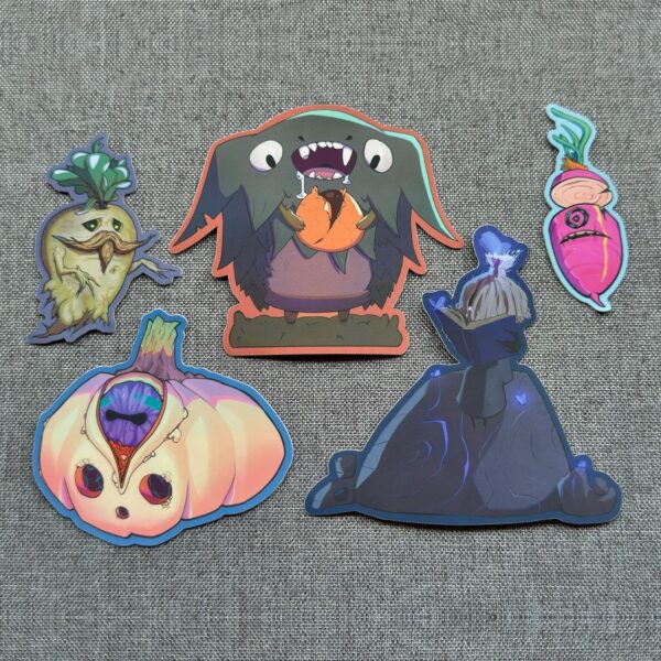 The five Mystic Garden stickers by Kor on gray fabric: Fredrik the Mandrake, Devon the Candy Thief, Benny the pink radish, Gus the one-eyed pumpkin, and Shien reading a book