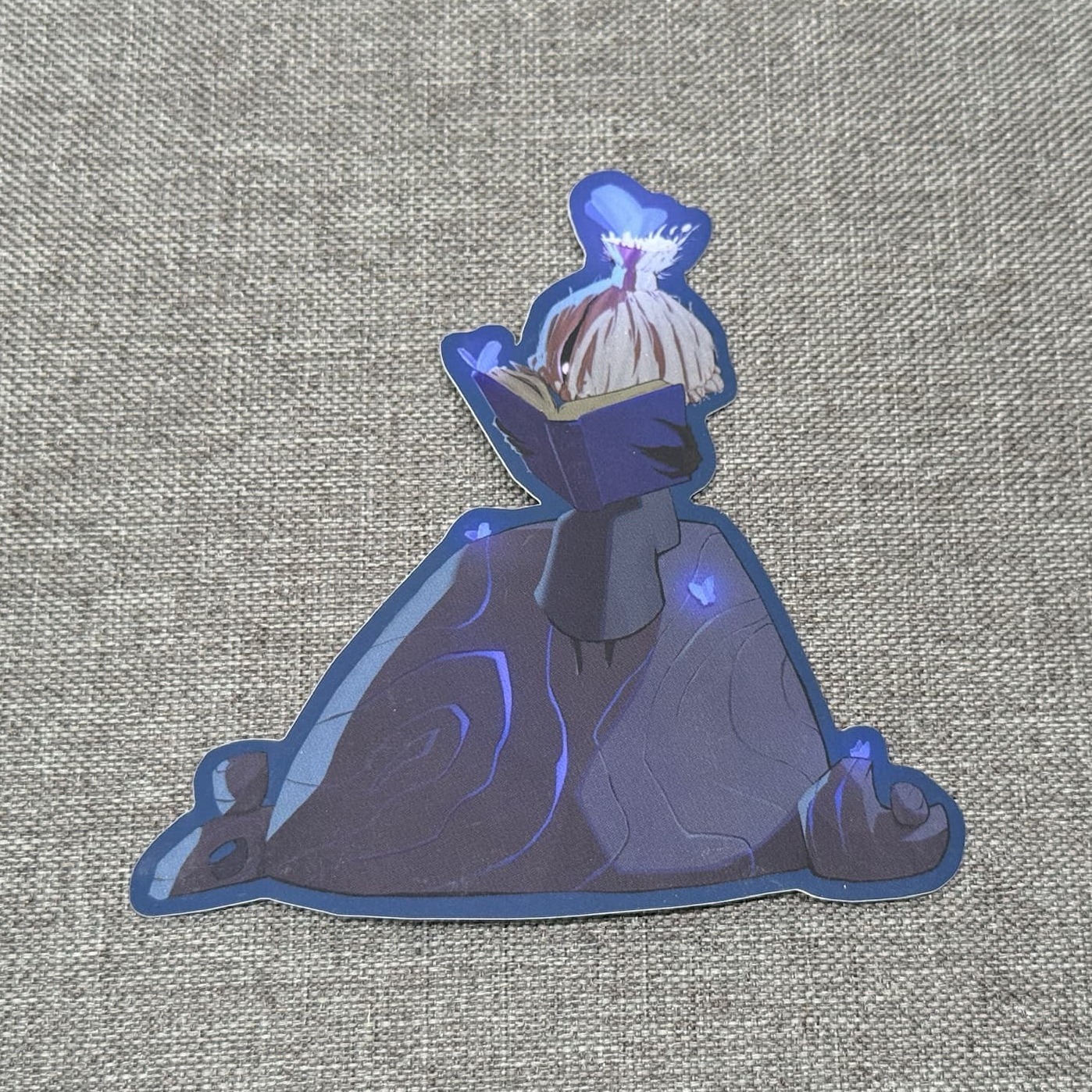 Shien sticker: a dark blue cloaked figure with a pale flame for hair, reading a book, outlined in blue