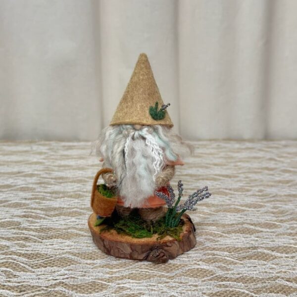 Tom, a handmade gnome with a tan felt hat, white hand-tied yarn beard, a basket of moss and beaded lavender plants on a wood slice base