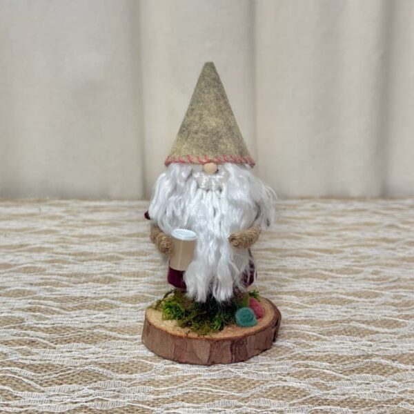 Zak, a handmade gnome with an oatmeal felt hat, white yarn beard, burgundy coat, holding a tiny coffee cup on a wood slice base